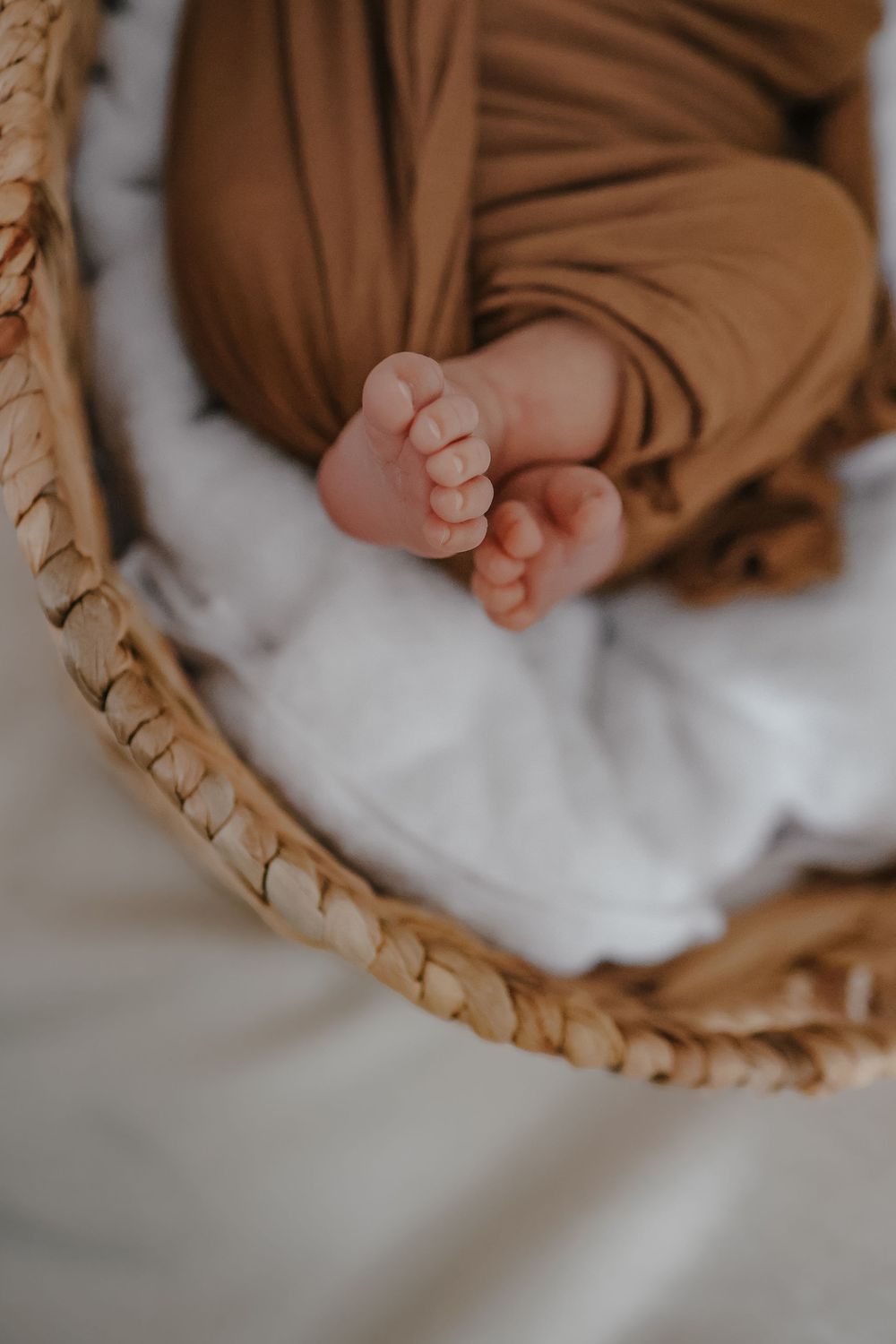 Close up of tiny baby feet and hands resting in a woven wicker basket with brown and white fabric.