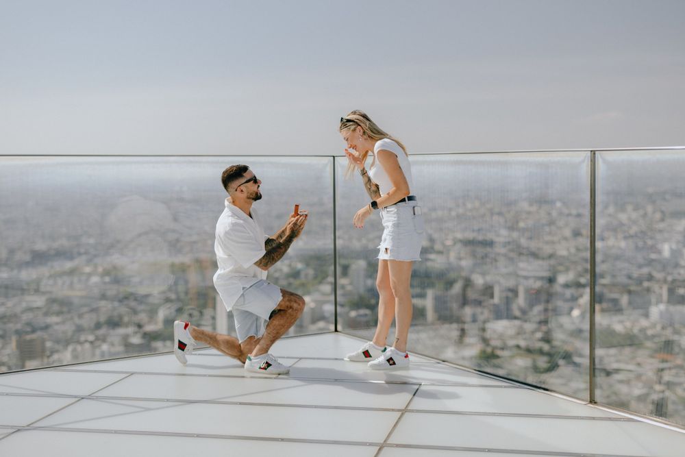 A romantic marriage proposal takes place on a scenic rooftop terrace overlooking a sprawling cityscape.