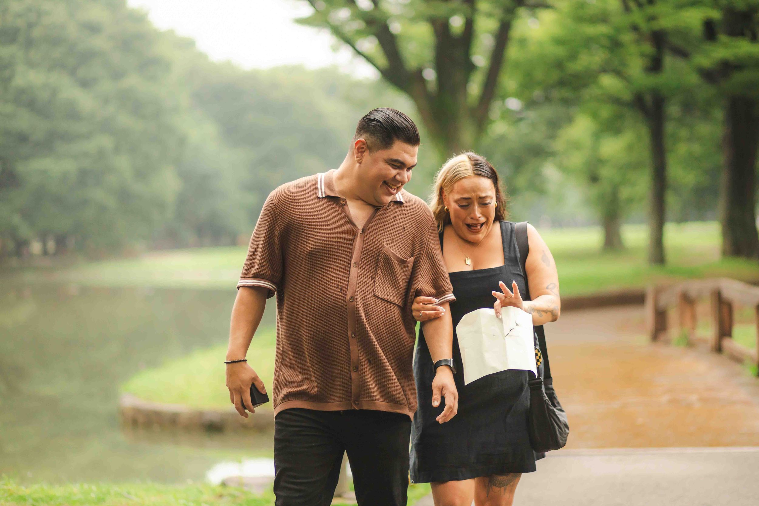 Happy couple laughing while walking together on park path near lake.