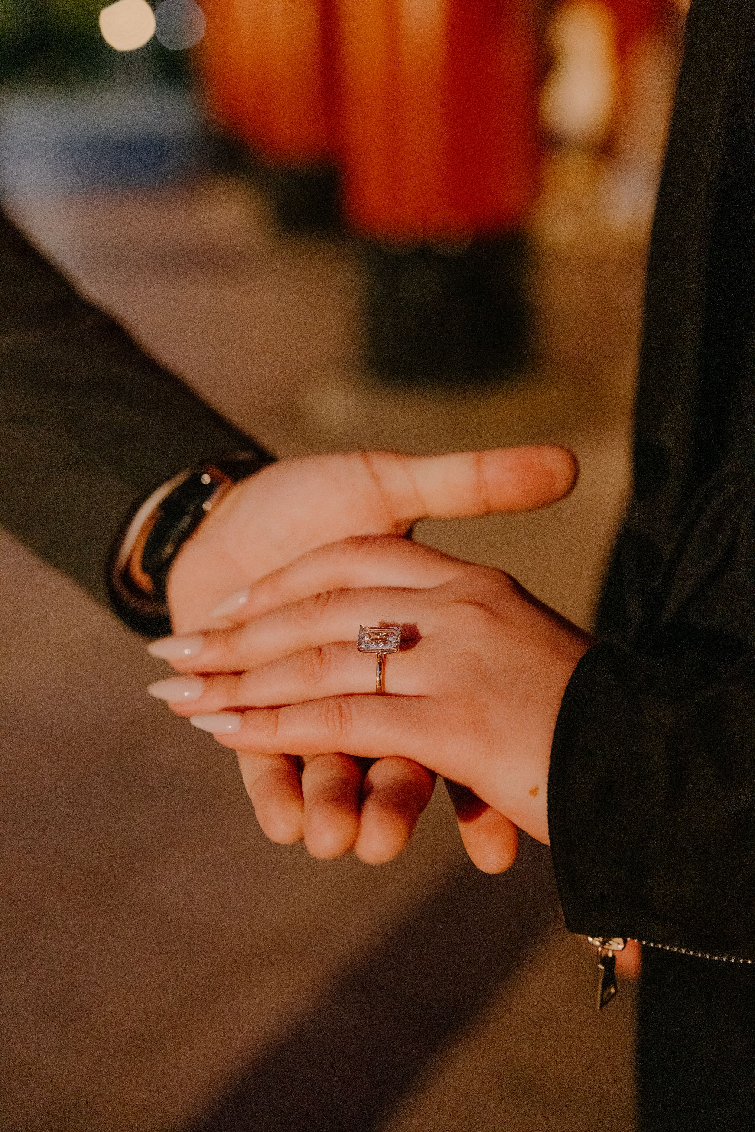 Close-up of hands wearing a sparkling engagement ring with a diamond solitaire in warm lighting.