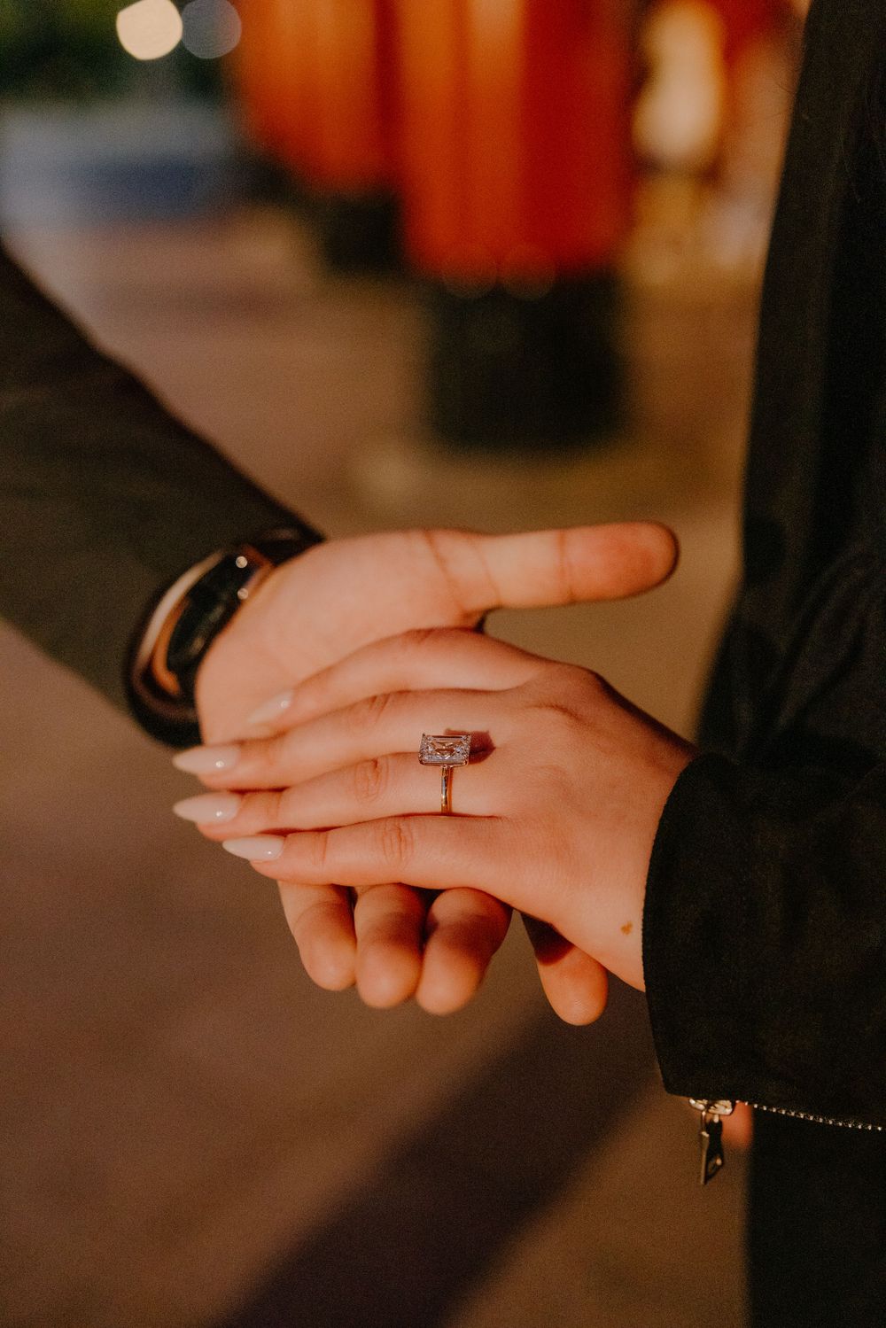 Close-up of hands wearing a sparkling engagement ring with a diamond solitaire in warm lighting.