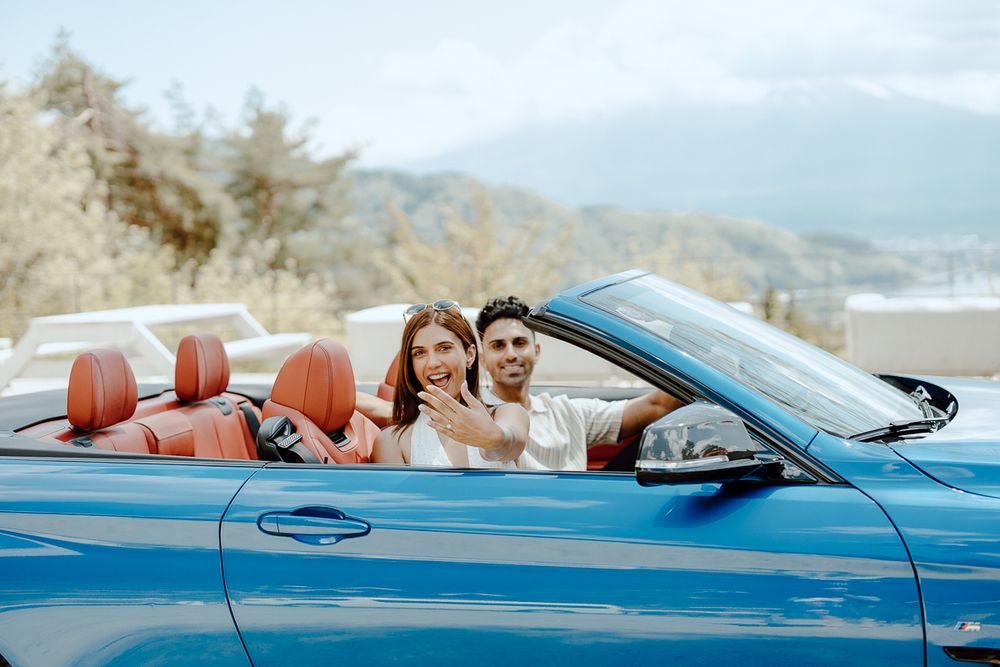 Happy couple enjoying ride in blue convertible car with mountain scenery.