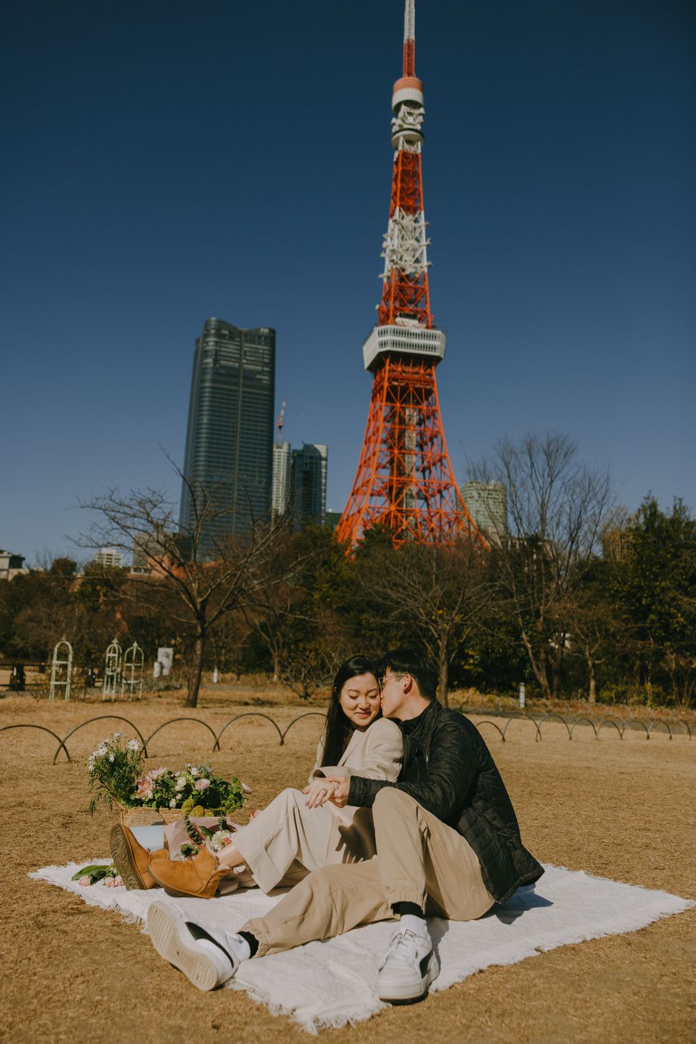 Couple enjoying romantic picnic on grass with Tokyo Tower and modern skyscrapers in background.