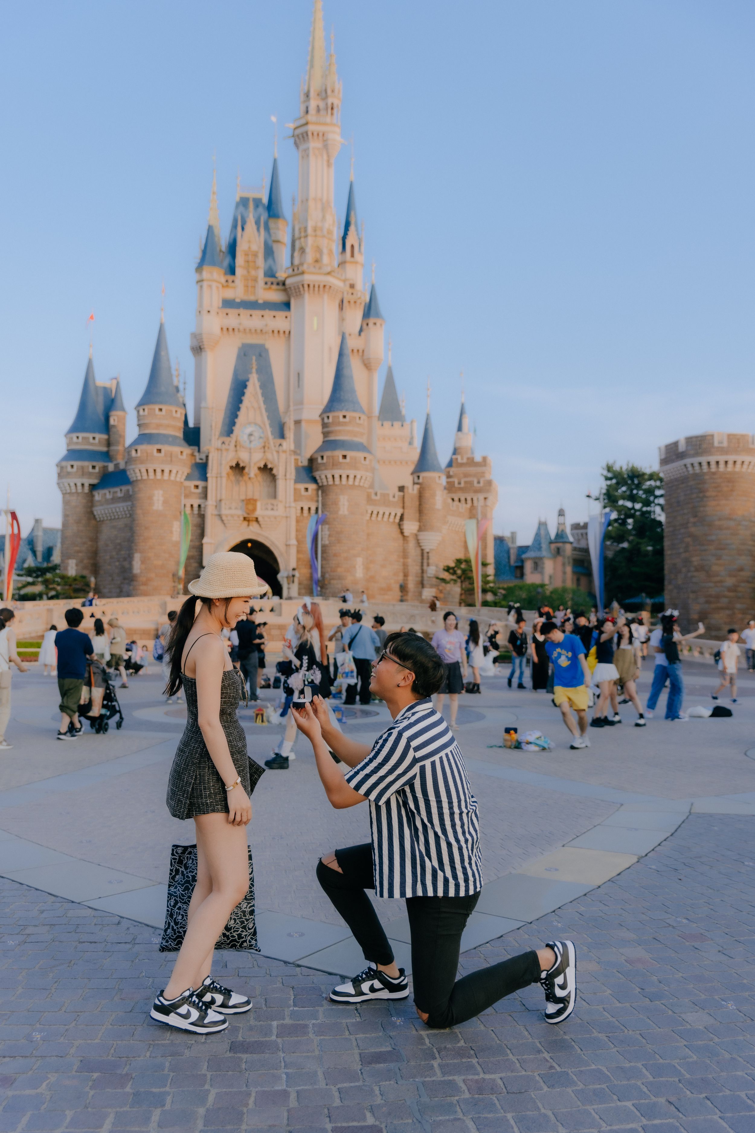 A romantic proposal takes place in front of Cinderella Castle at Disney World with crowds gathered around.