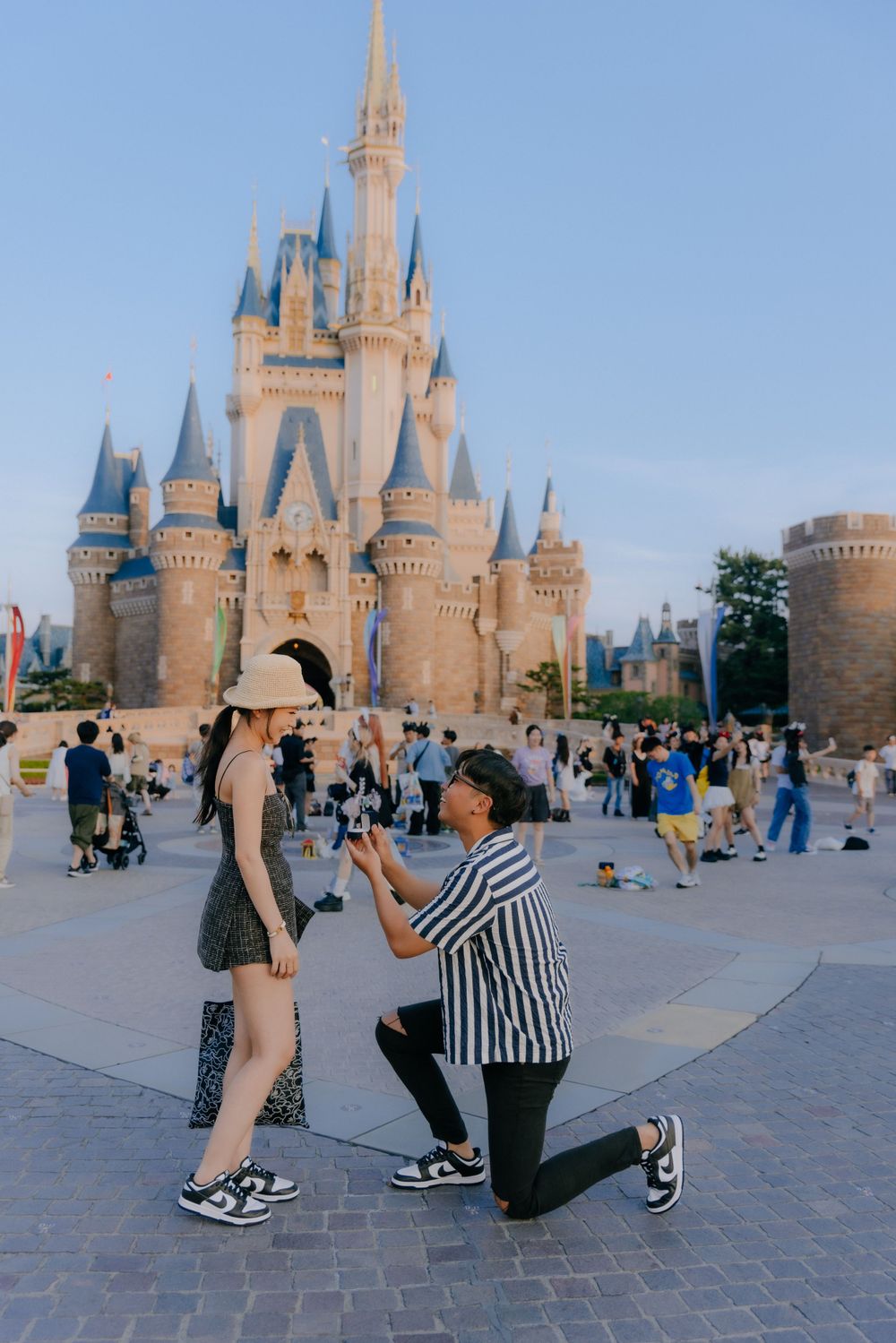 A romantic proposal takes place in front of Cinderella Castle at Disney World with crowds gathered around.