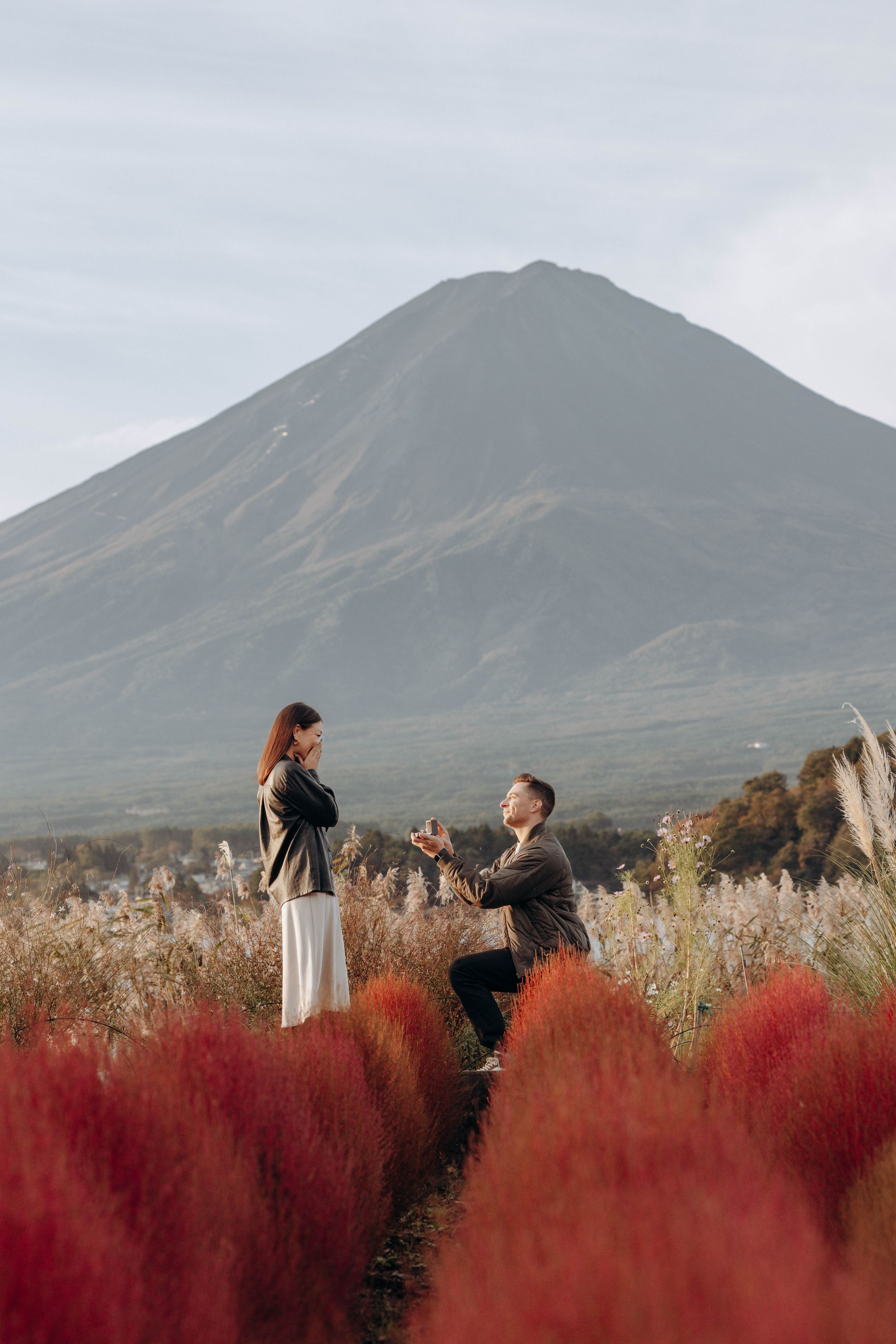 A proposal scene with a majestic mountain backdrop and red autumn foliage in the foreground.