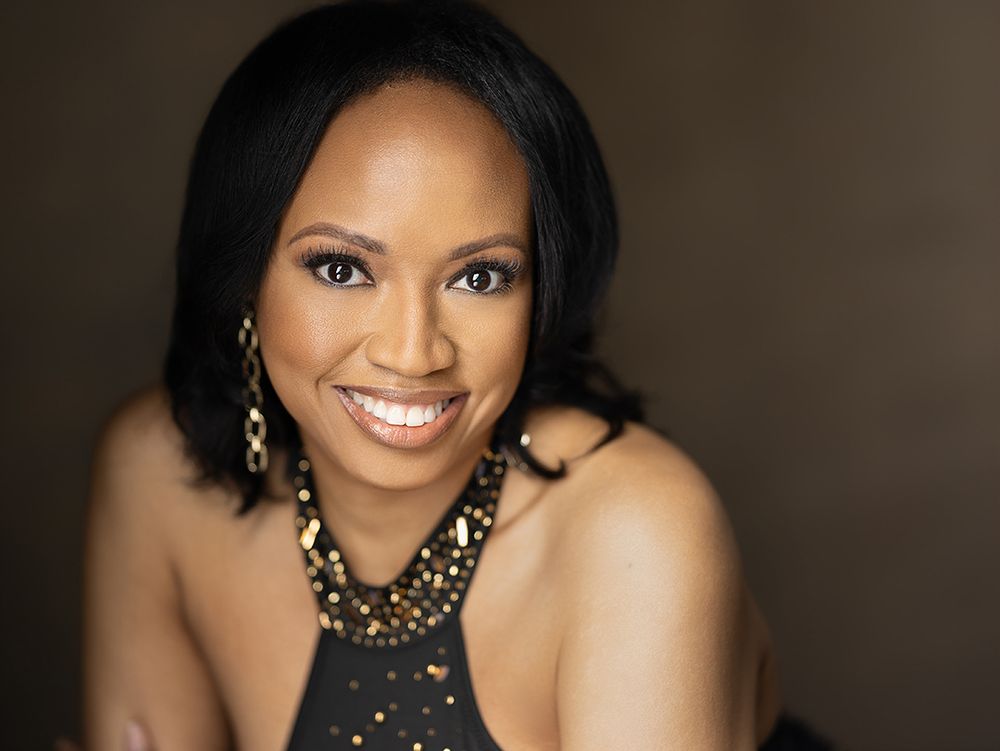 Smiling woman with short black hair wearing gold earrings and a sparkly top poses for a professional headshot.