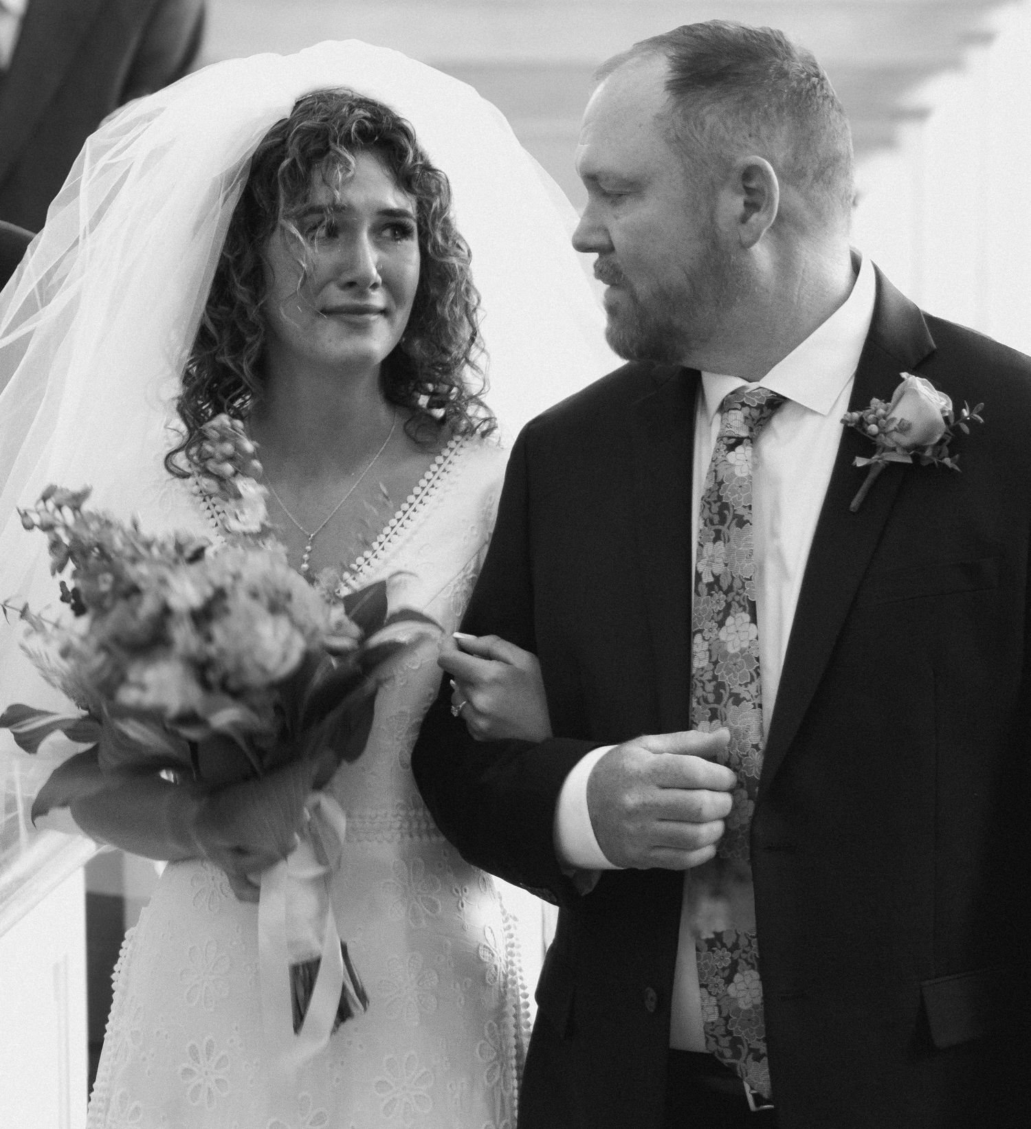 A wedding couple shares a tender moment while holding a bouquet of flowers.