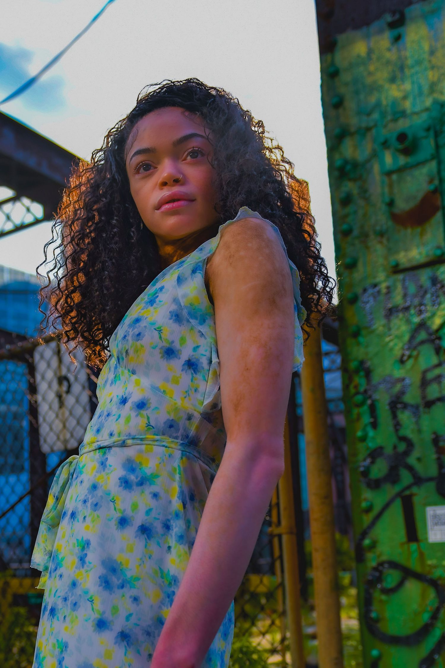 Low angle portrait showcasing a floral summer dress against an urban industrial setting.