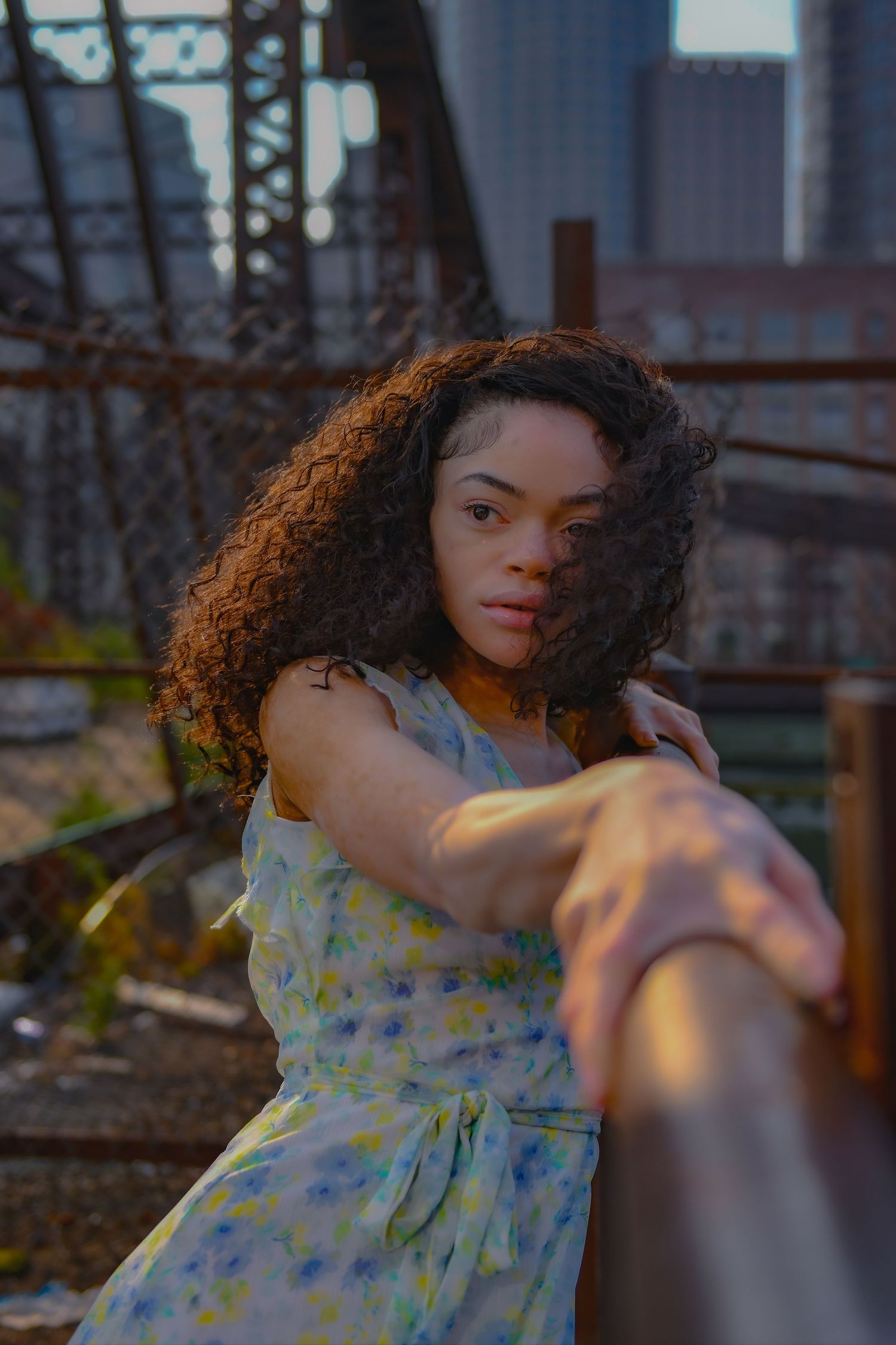 Sunset portrait in floral dress near urban bridge structure.