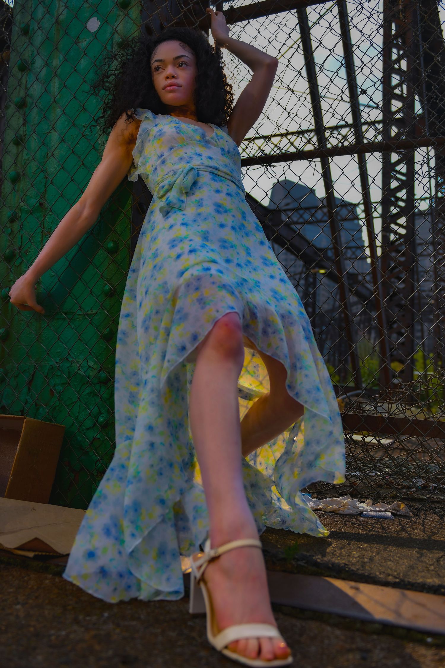 Fashion pose in flowing floral dress against industrial urban backdrop.