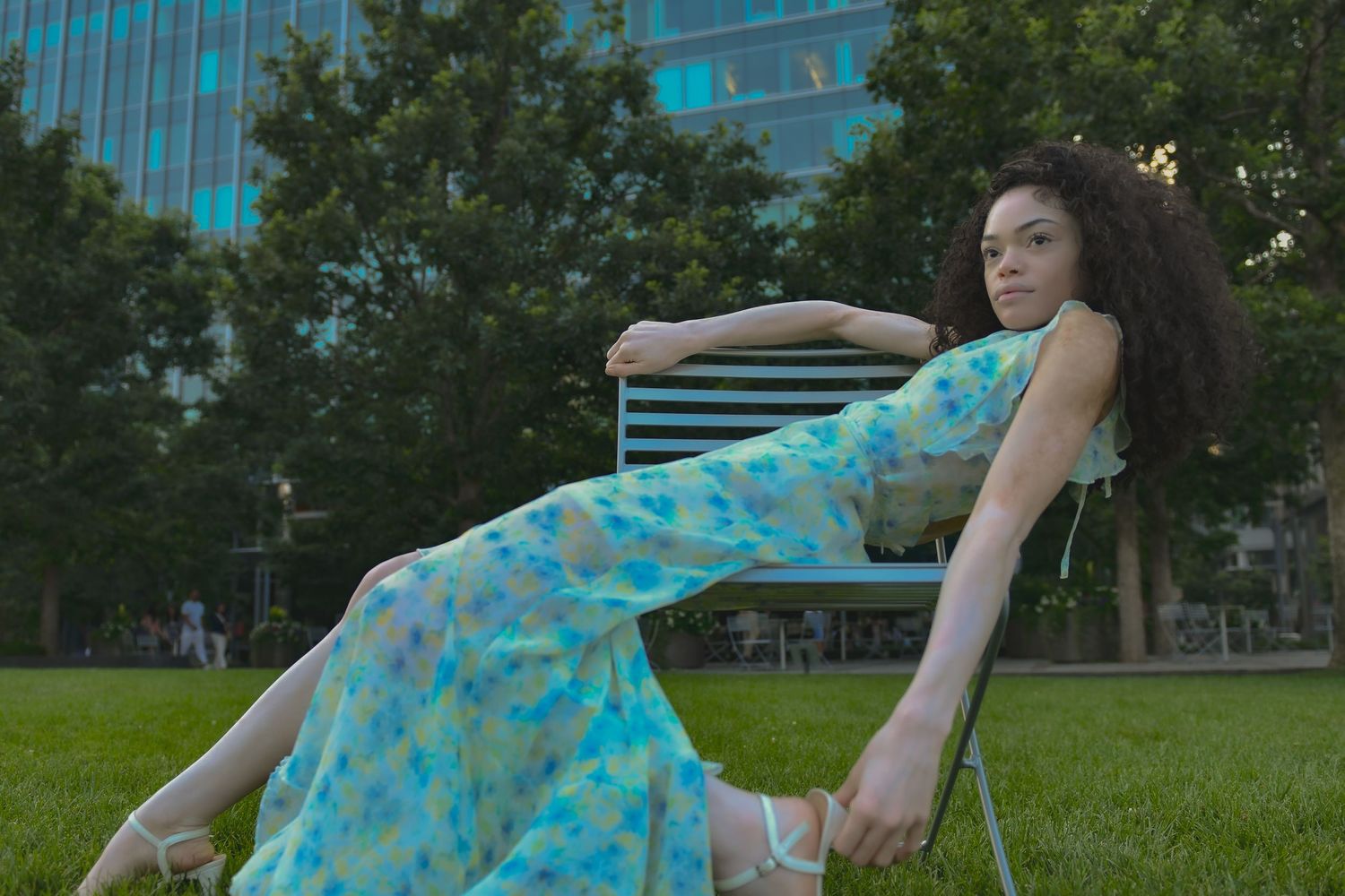 Relaxed summer fashion pose in a floral dress while lounging on a chair outdoors.