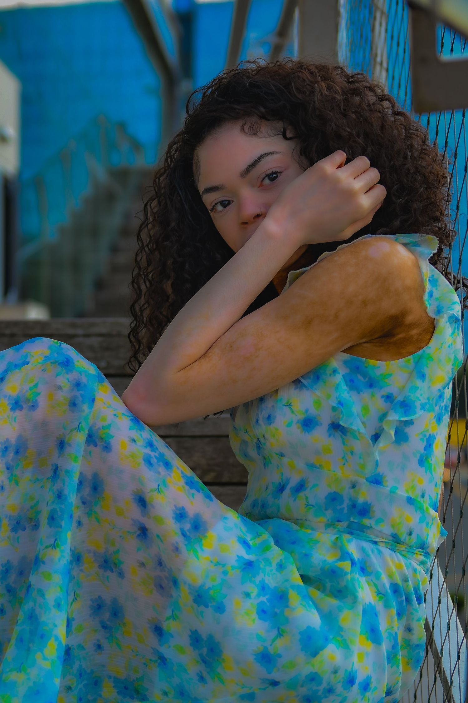 Fashion portrait of someone in a blue and yellow floral dress posing against a vibrant blue urban backdrop.
