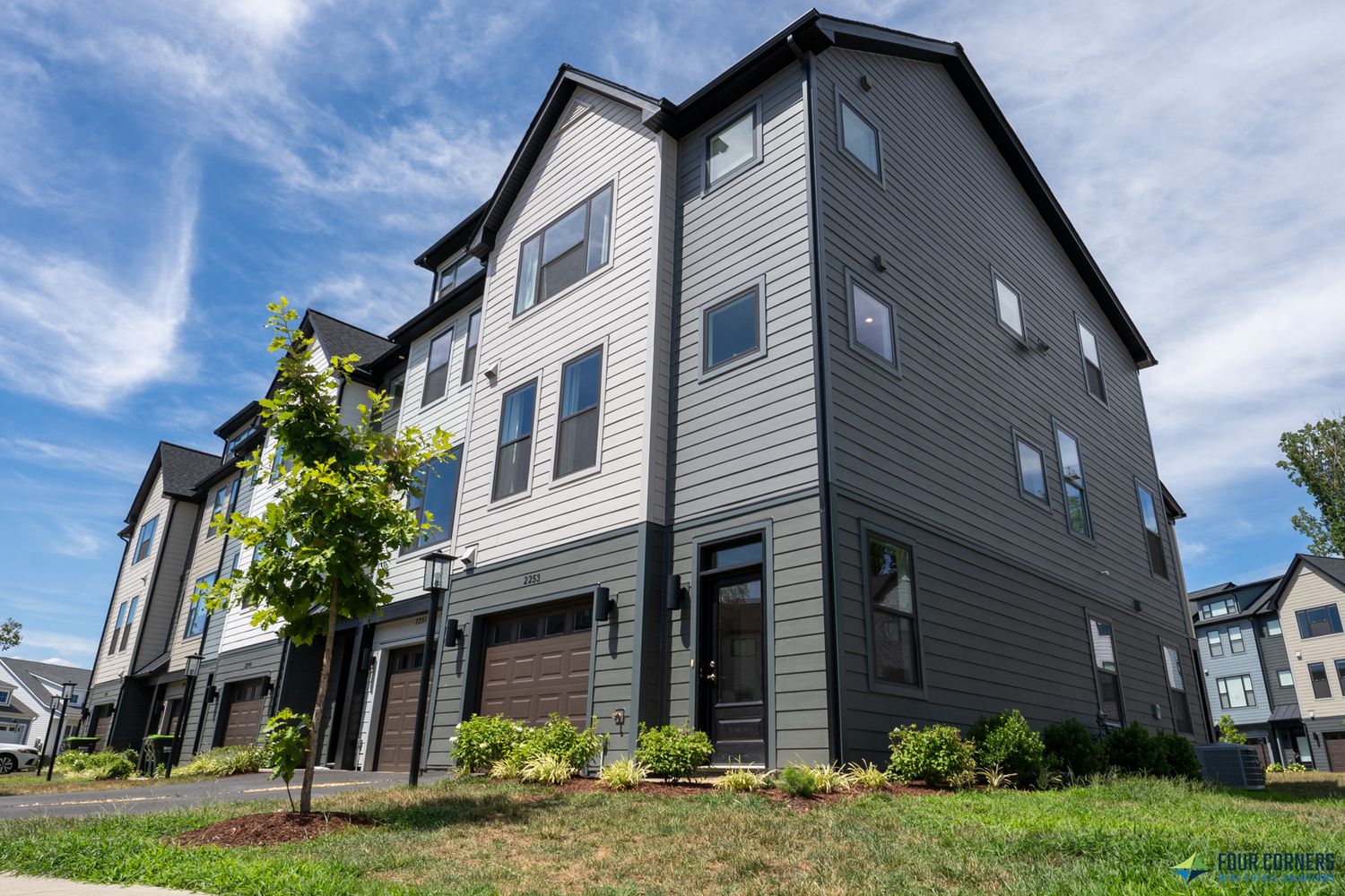 Modern gray siding townhomes with white trim shown from multiple angles on a grassy hillside under blue skies.