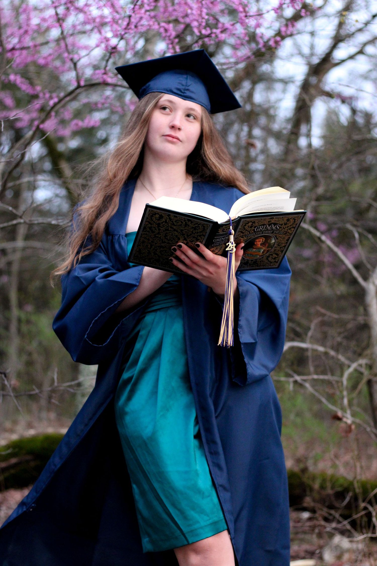 Senior smiling and looking away from the camera with cap and gown with book.