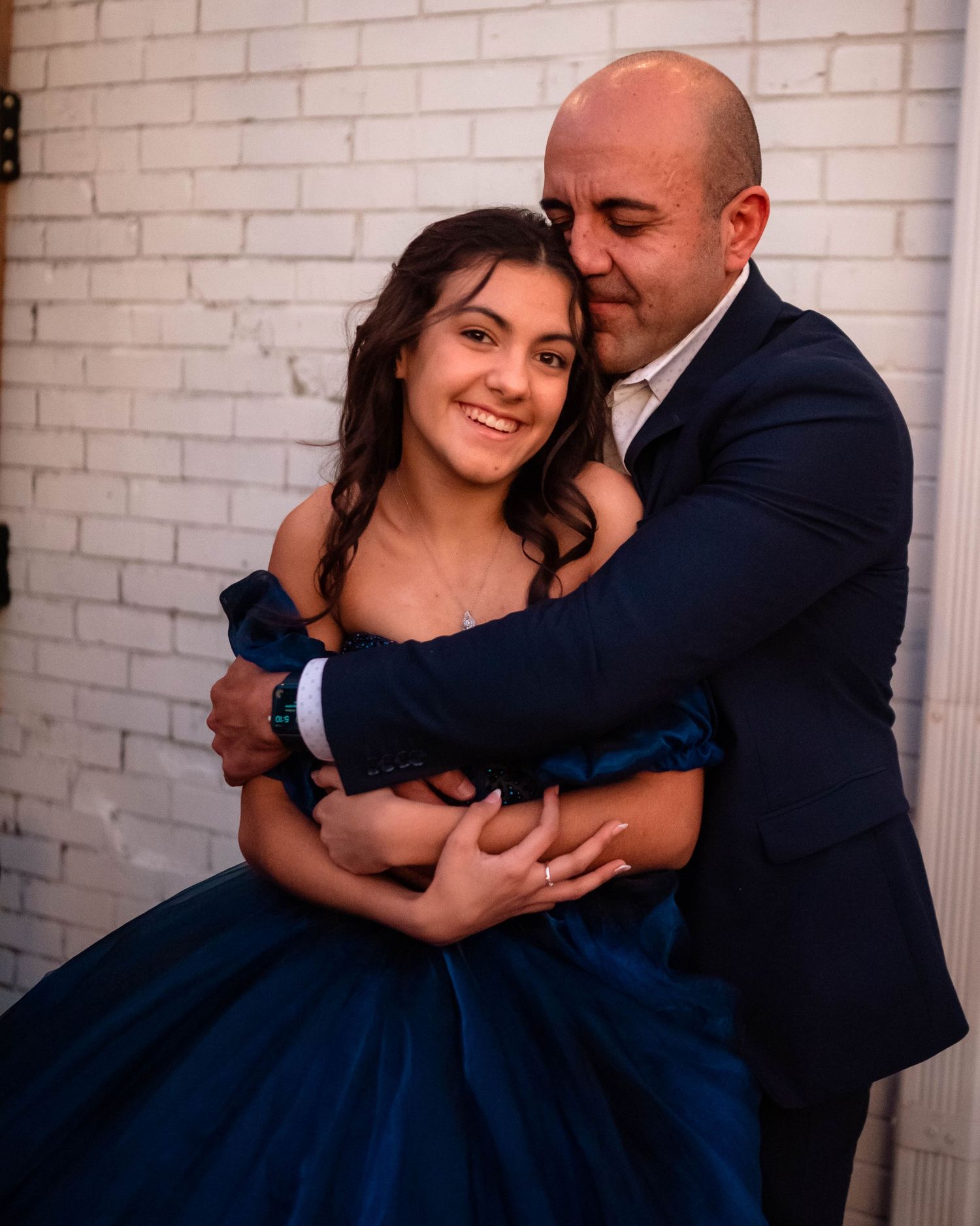 Romantic couple embraces while dancing, with the woman wearing an elegant navy blue ball gown.