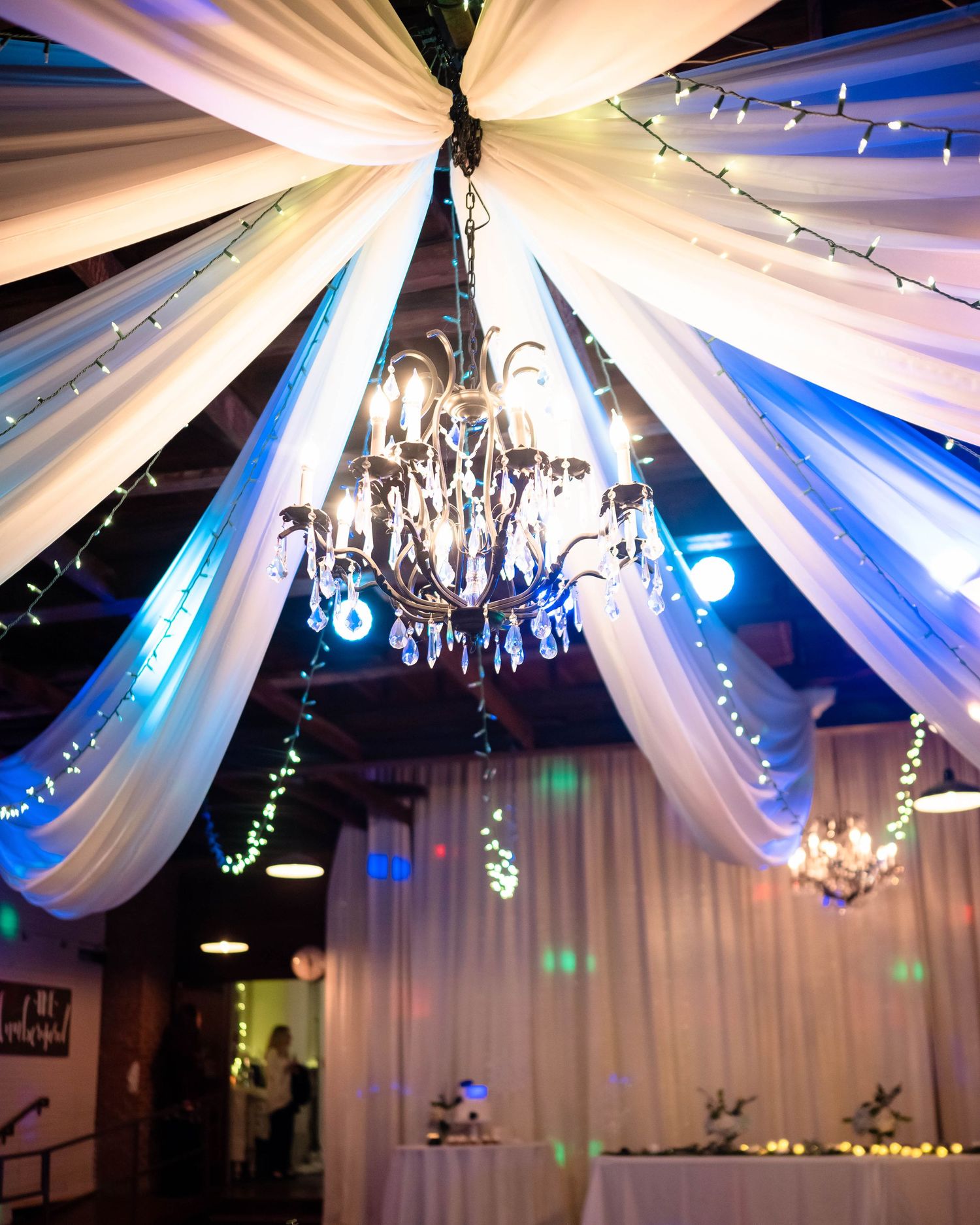 Elegant reception hall decorated with white fabric draping and crystal chandeliers.