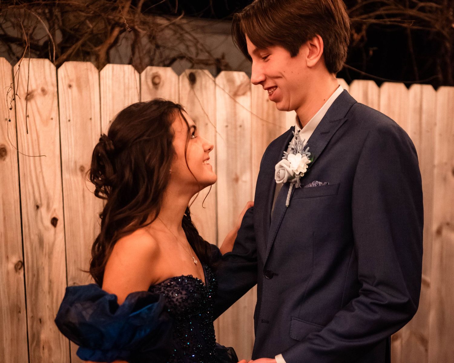Couple in formal wear sharing intimate moments against rustic wooden backdrop.