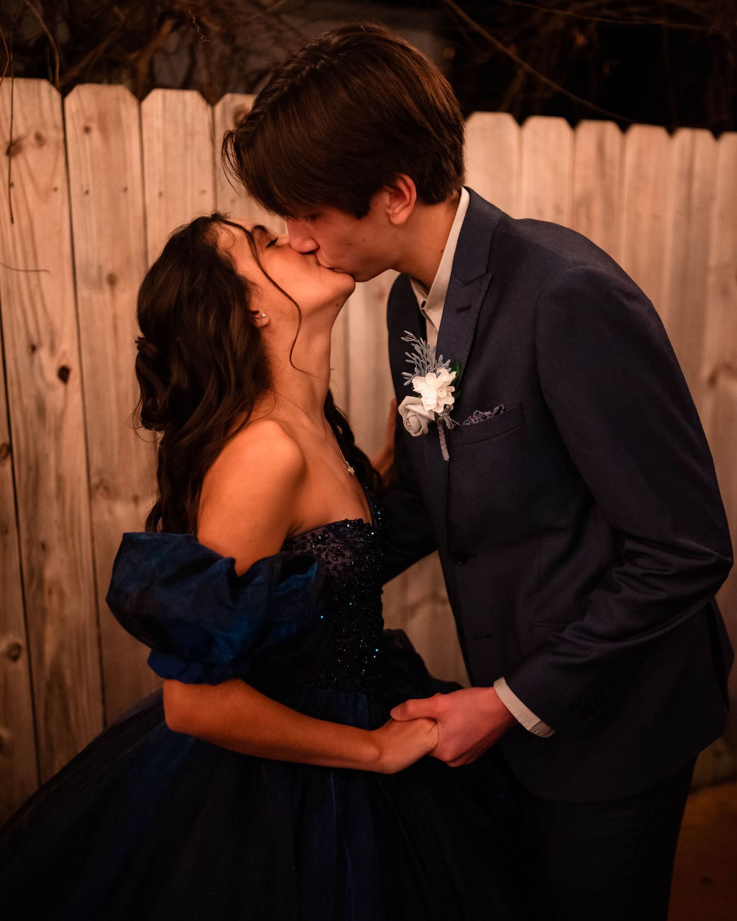 Dancing couple in formal attire against wooden fence backdrop.
