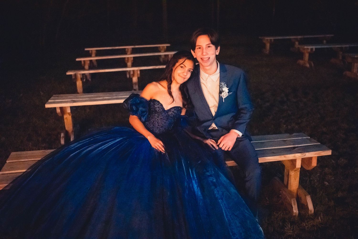Couple poses on rustic wooden bench during evening photo session with romantic lighting.