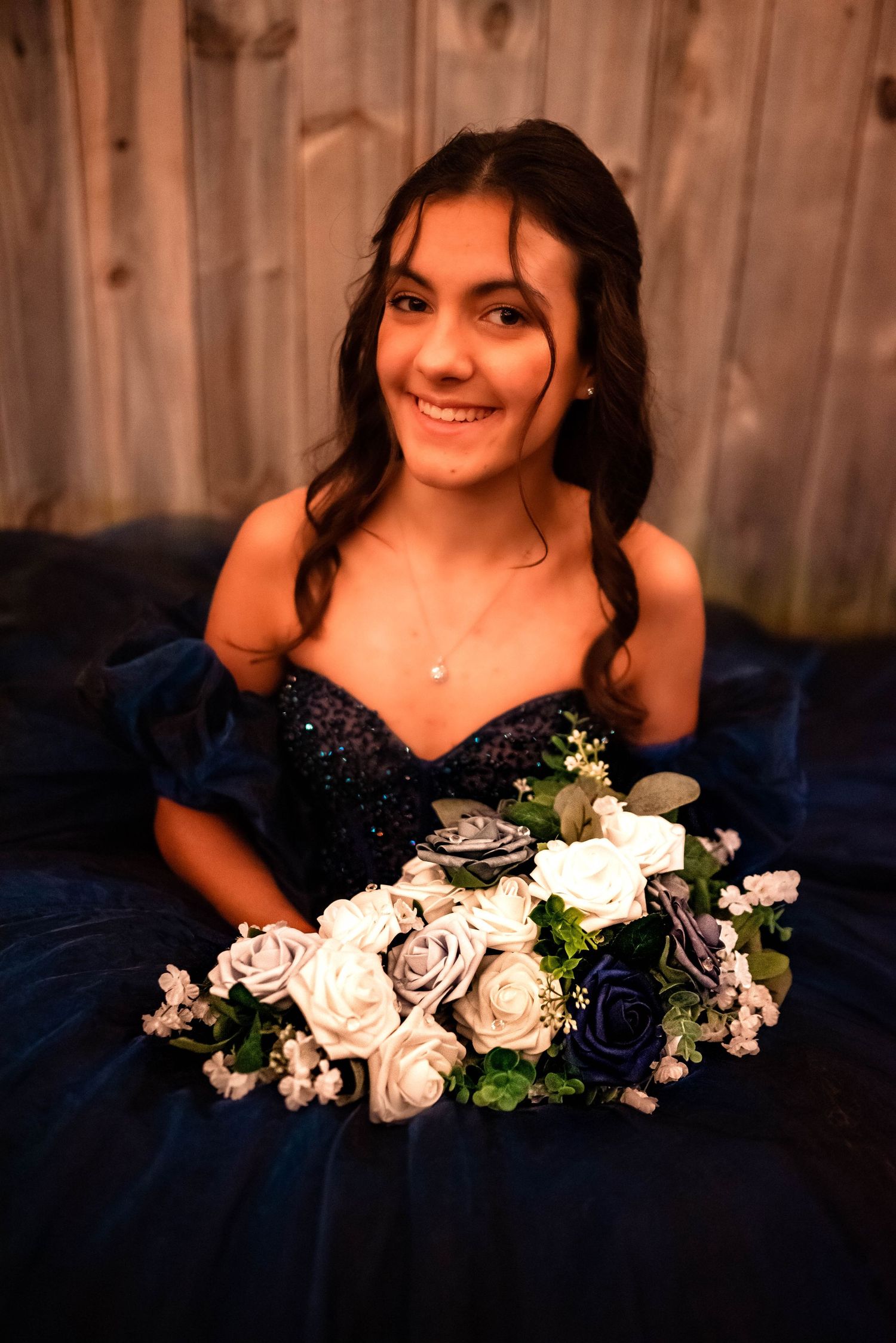 Navy blue gown with floral bouquet of white and silver roses against dark background.