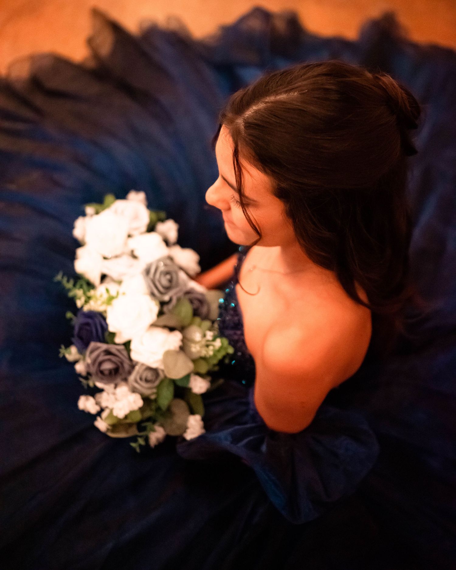 Artistic portrait with navy dress and floral bouquet in warm lighting.