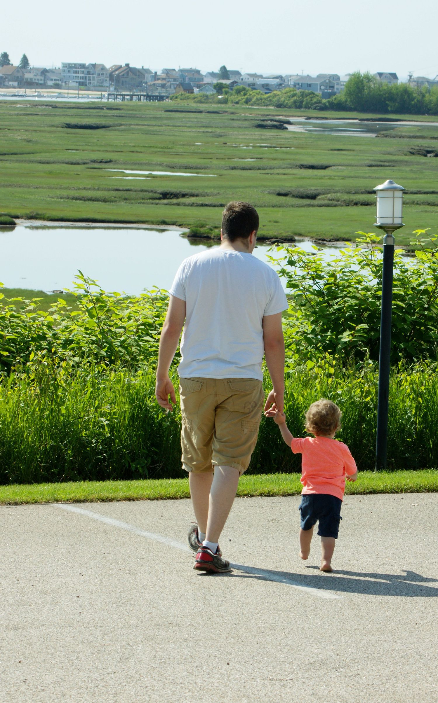 Two people walking on a path overlooking green wetlands and water on a sunny day.