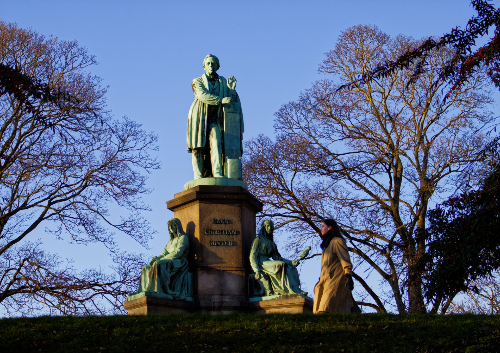 Photo of monument for H.C Ørsted, Copenhagen. A young woman passing looks as if she might be part of the monument.