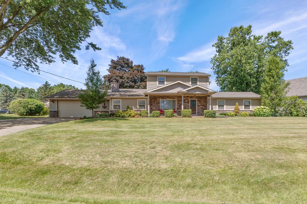 Large two-story brick and tan home with covered entry, manicured landscaping, and expansive green lawn.
