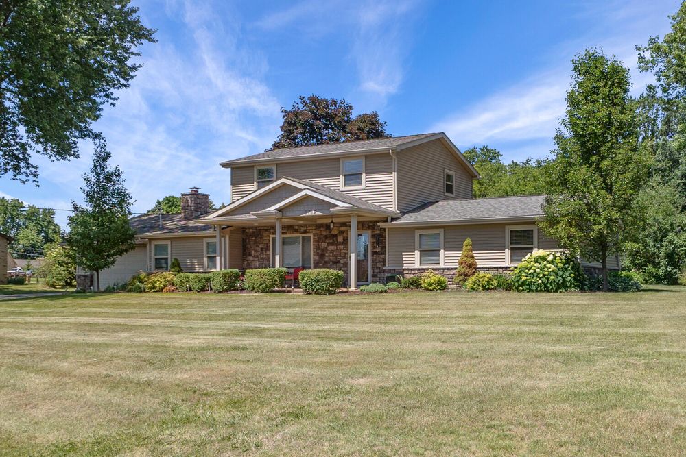 Spacious two-story home with brick accents, covered porch, mature trees, and neatly trimmed front lawn.