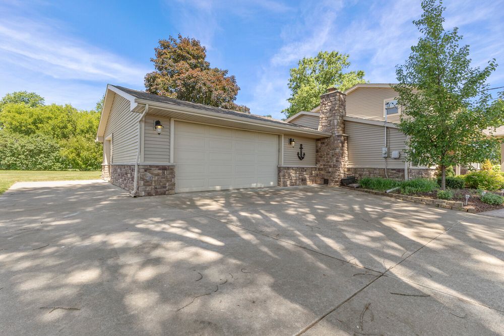 Two-car garage with stone accents and wide concrete driveway leading to a two-story home.