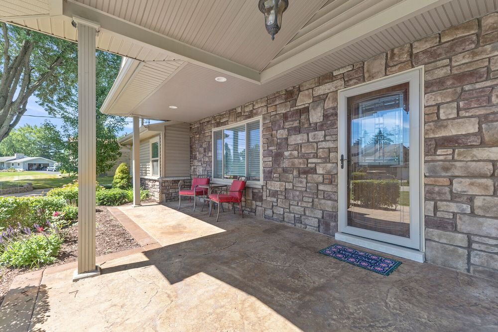 Covered stone patio entrance with decorative ceiling, red chairs, and stamped concrete flooring.