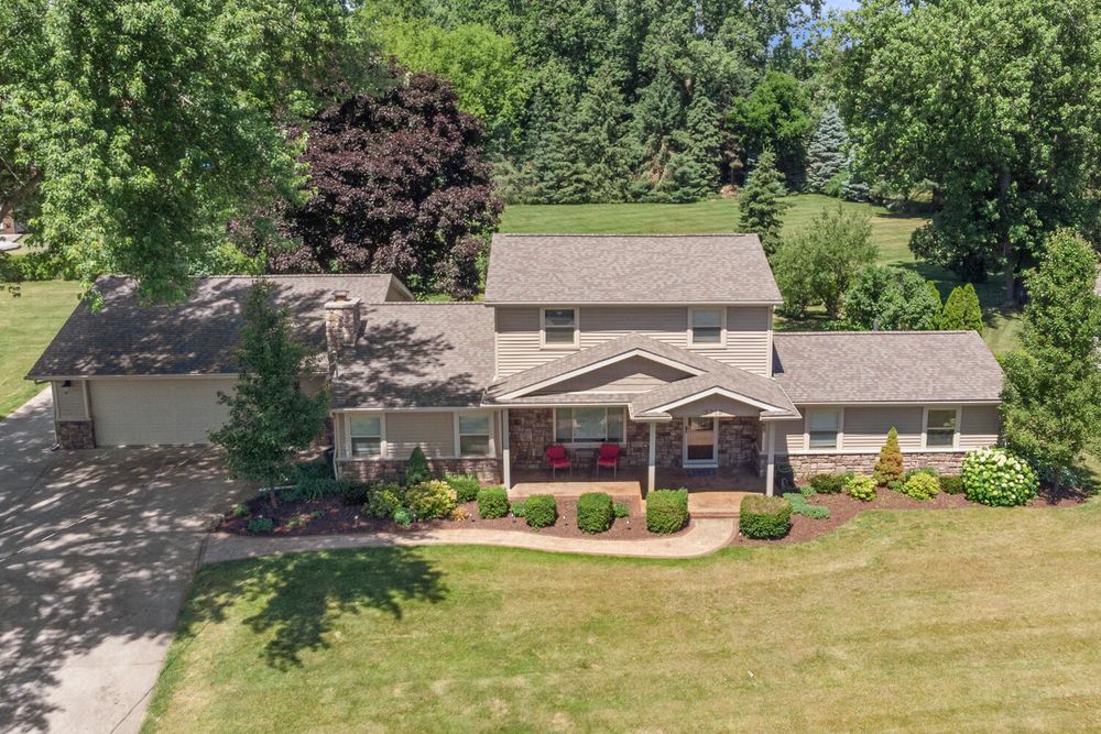 Aerial view of two-story home with brick porch, attached garage, and large landscaped yard.