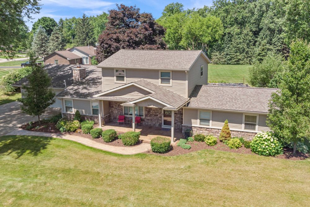 Aerial view of two-story home with stone accents, covered porch, attached garage, and lush landscaping.