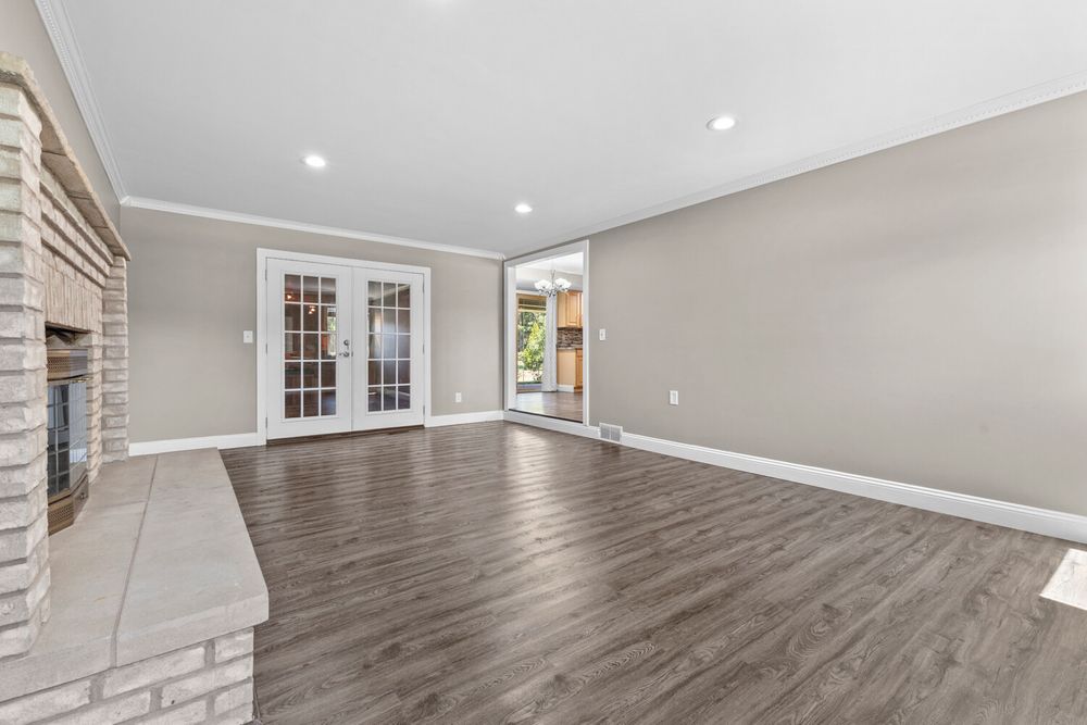 Open living room with brick fireplace, dark hardwood floors, French doors, and abundant natural light.