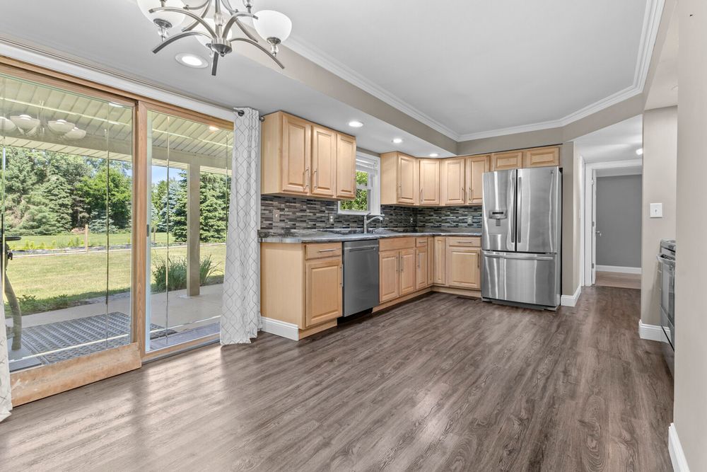 Modern kitchen with light wood cabinets, stainless steel appliances, tile backsplash, and sliding glass door.