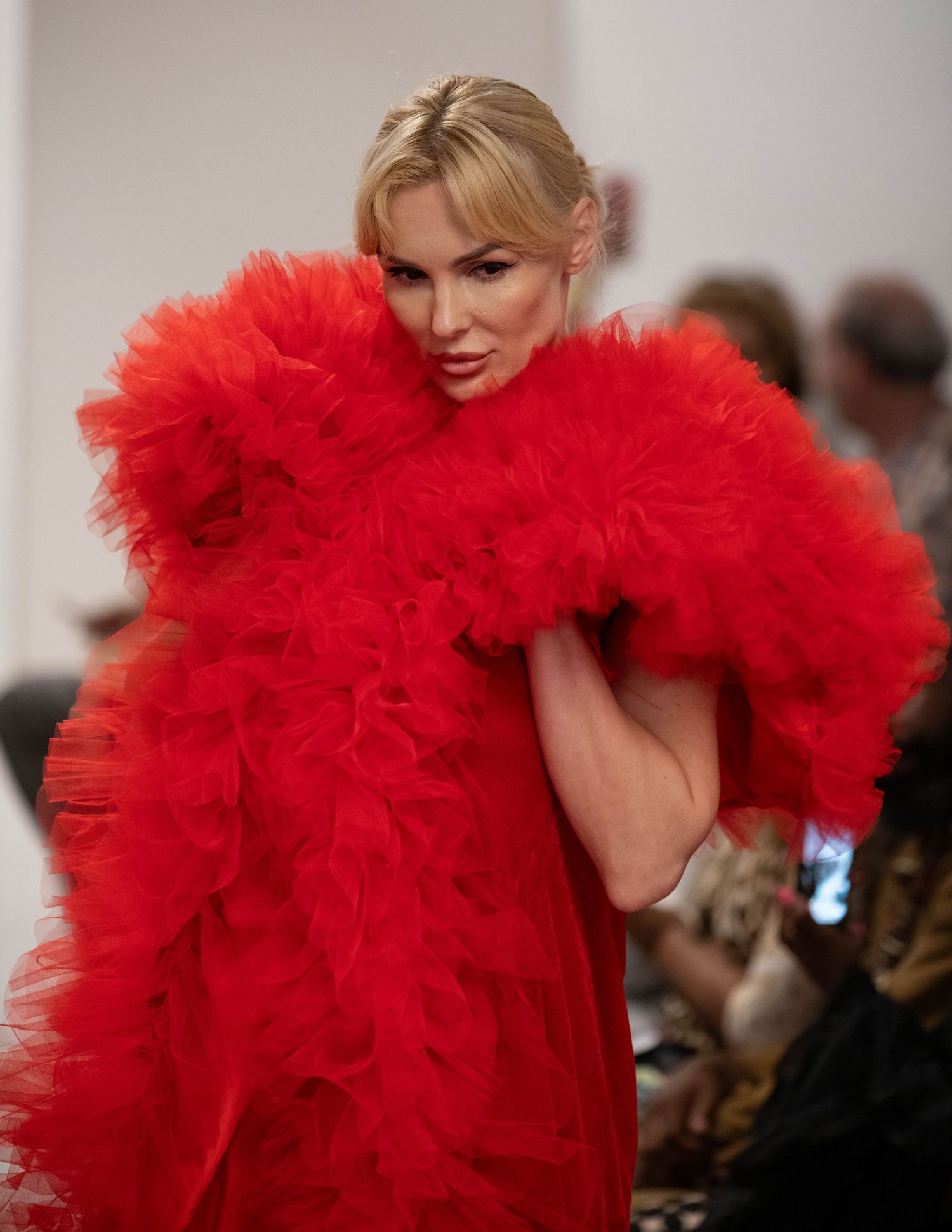 Model wearing dramatic red tulle gown on fashion runway.