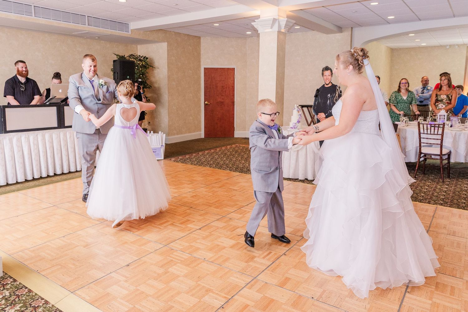 Wedding reception dance floor scene showing joyful interactions between bridal party members.