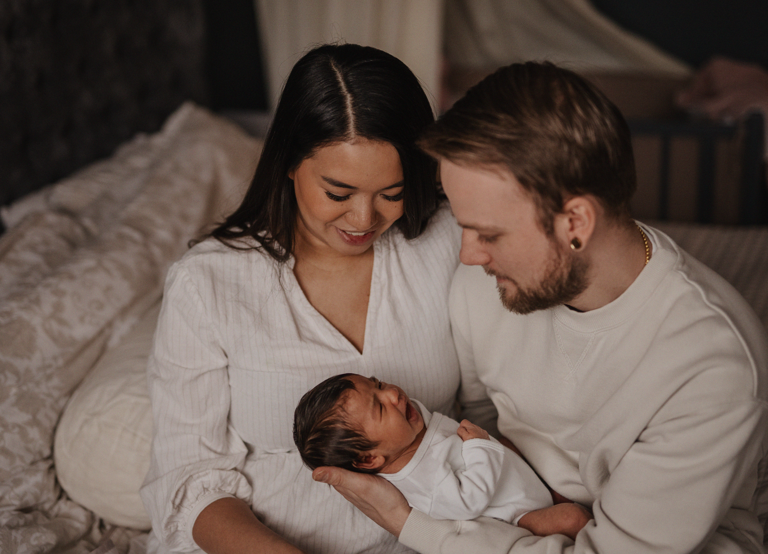 Intimate indoor family moment with a newborn baby in soft lighting.