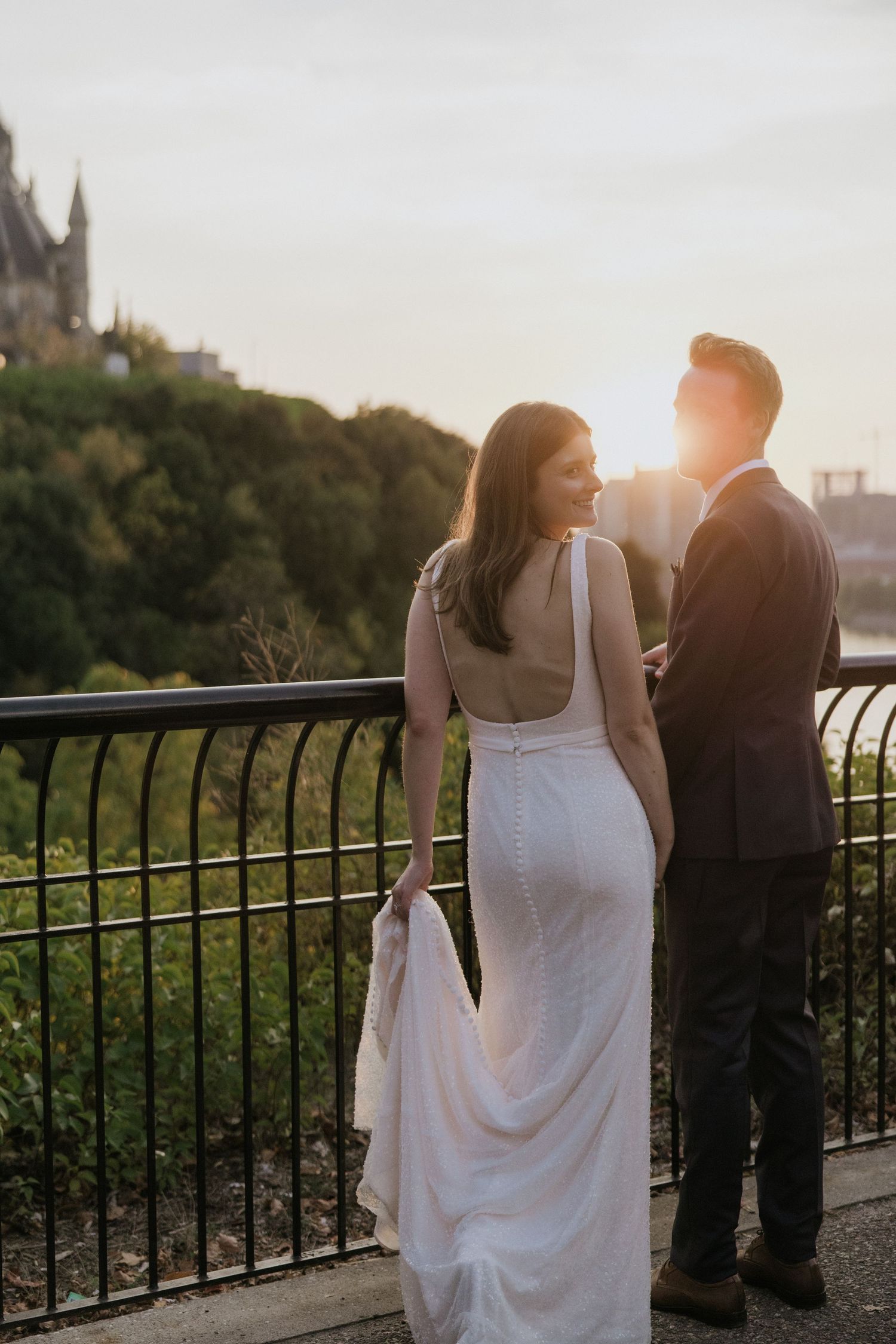 Newlyweds pose romantically on wooden dock overlooking ocean at sunset.