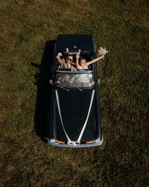An aerial view of a classic black car with people celebrating inside.
