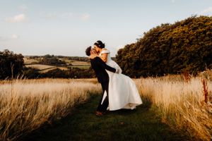 A joyful wedding couple embracing in a golden sunlit field.