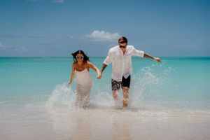 Happy couple playing and splashing in shallow turquoise waters on tropical beach.