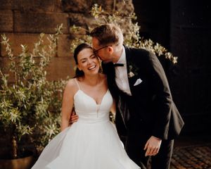 Couple shares intimate laughing moment against brick wall with floral decorations.