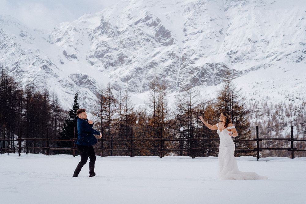 Couple playfully posing in snowy mountain landscape during winter wedding shoot.