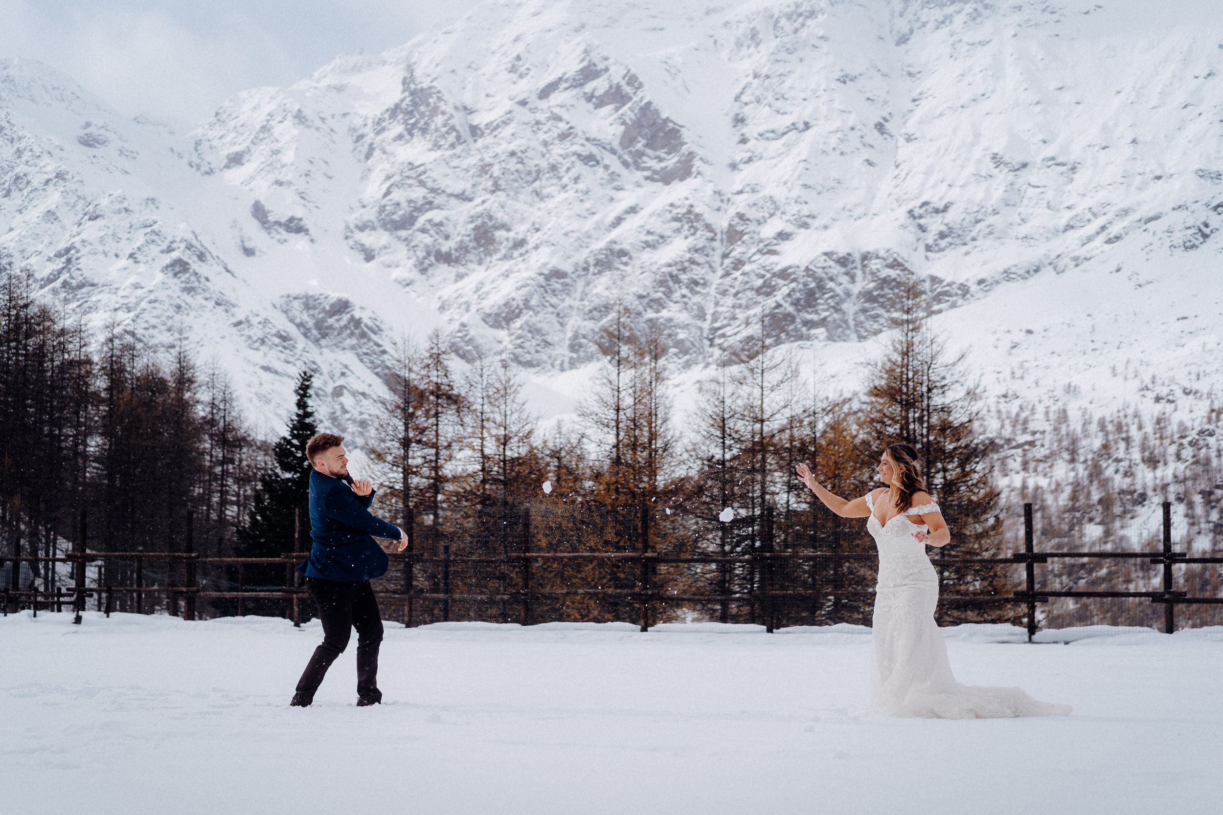Couple playfully posing in snowy mountain landscape during winter wedding shoot.