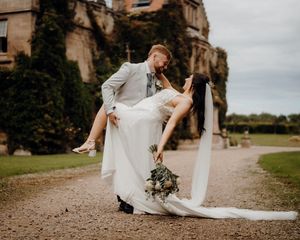 Romantic wedding couple dancing and posing together on gravel path outside historic stone building.