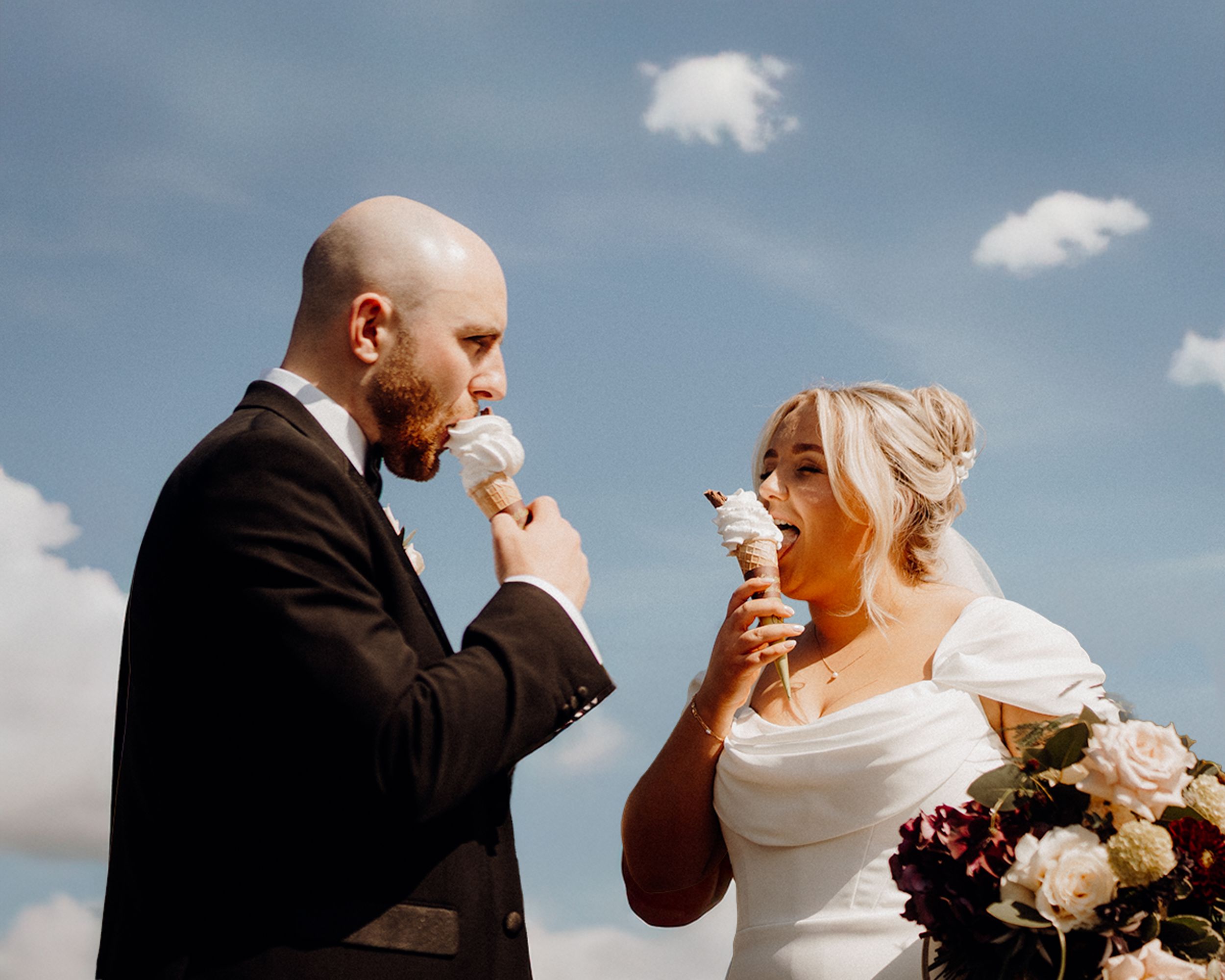 A romantic bride and groom share a tender moment against a blue cloudy sky during their outdoor wedding.