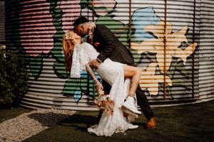 Romantic couple in wedding attire sharing an intimate dip pose against an industrial wall with graffiti.