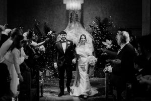 A joyous moment as newlyweds walk down the aisle while guests shower them with flower petals in a black and white photo.